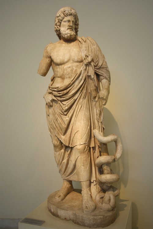 Estátua de Asclépio, cópia romana de um original grego do século 4 a.C., presente no Santuário de Asclépio em Epidauro.  Museu Arqueológico de Atenas. Via Wikimedia Commons.